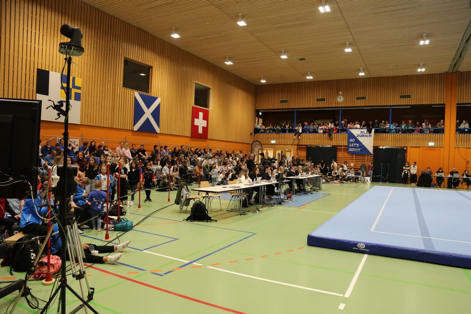 Turnhalle mit Zuschauern und Wettkampffläche.