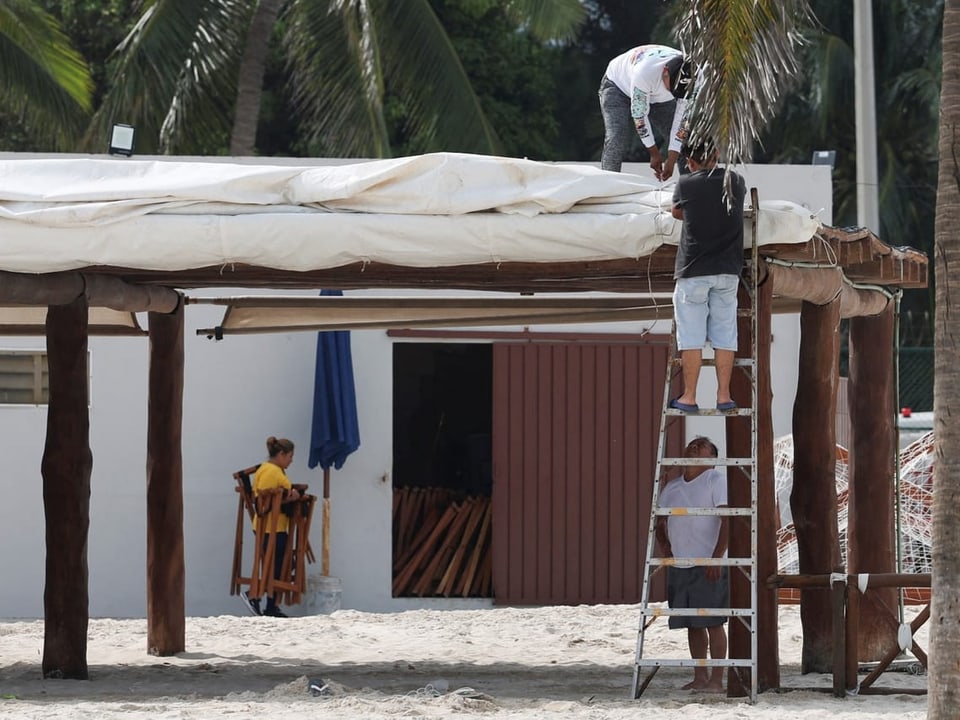 Zwei Männer auf Leiter reparieren Strandbar-Dach.