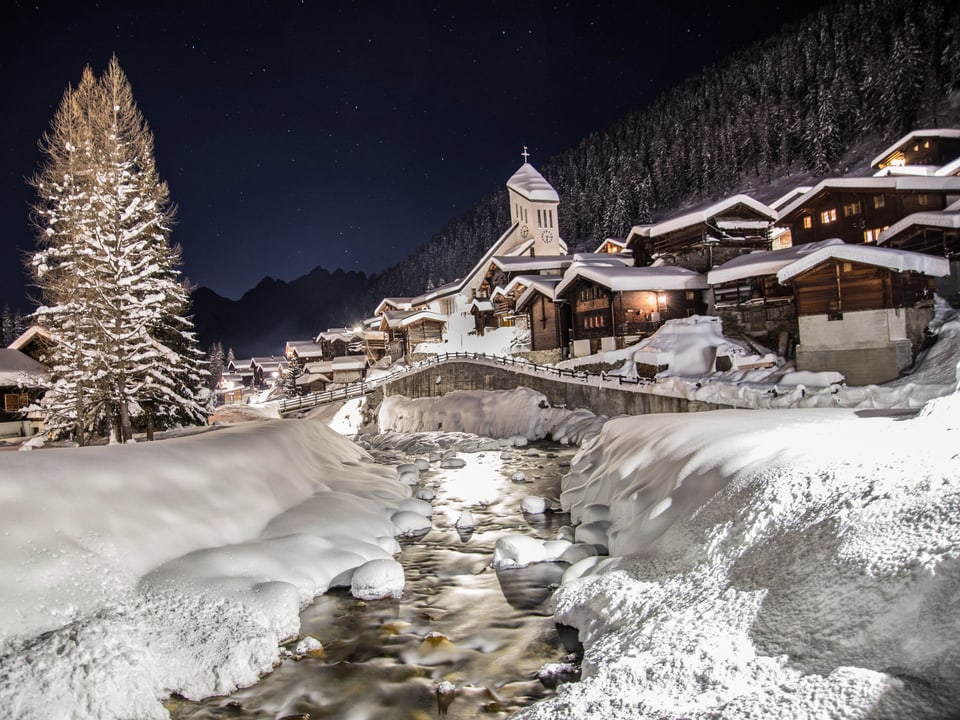 Blick aufs hell erleuchtete Dorf Blatten inmitten einer Winternacht.