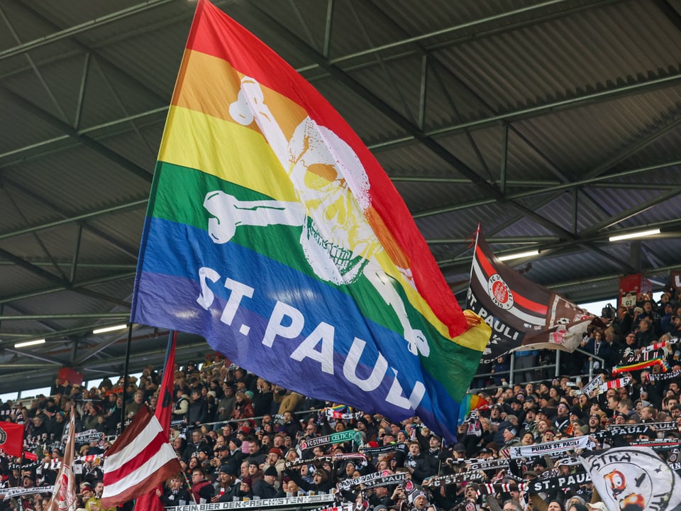 Regenbogenpiratenflagge im Fussballstadion mit Fans.