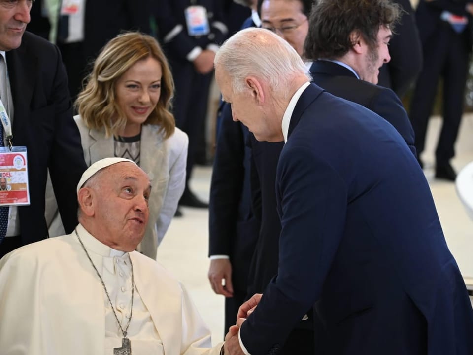 The Pope shakes the hand of a man in a suit.