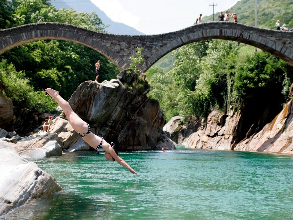 Eine Frau springt von einem Stein in die Verzasca.