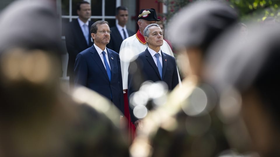 Herzog und Cassis stehen nebeneinander. Vor ihnen stehen Personen in einer Militäruniform.