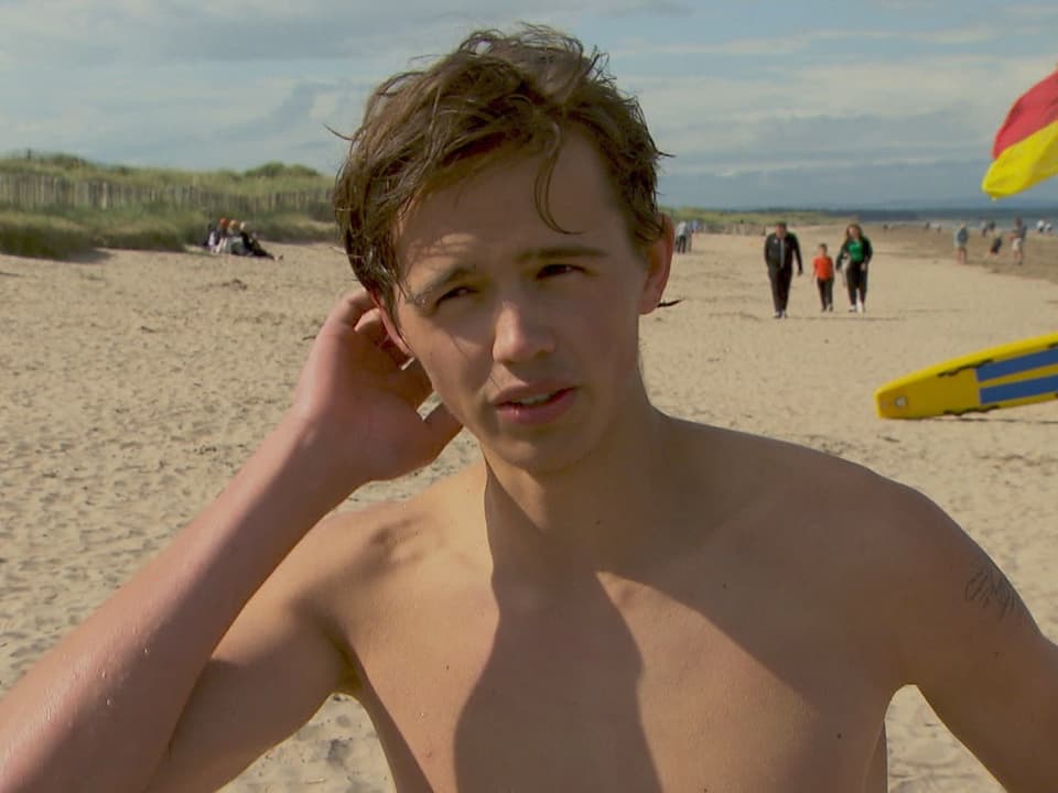 Mann am Strand mit Rettungsbrett im Hintergrund.