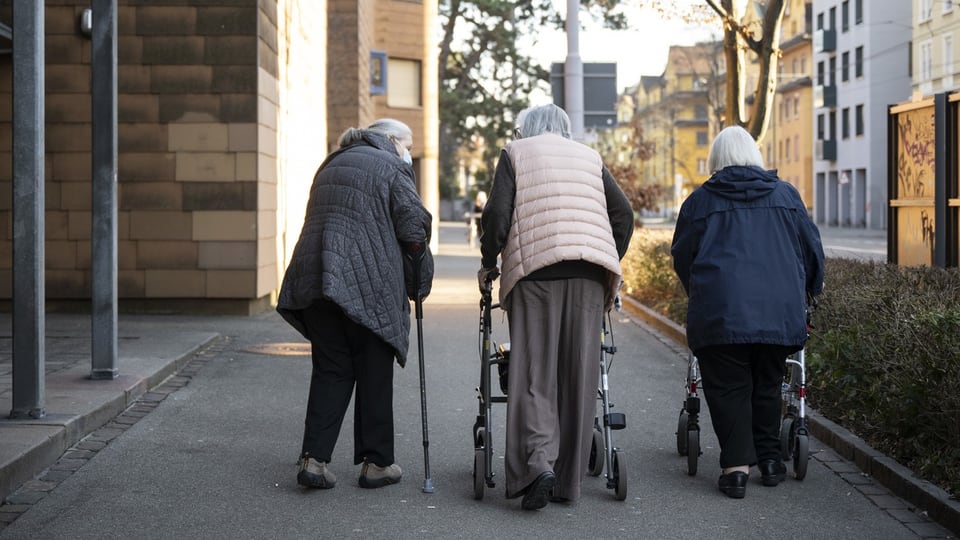 Drei ältere Frauen gehen mit Gehhilfen auf einem Gehweg.