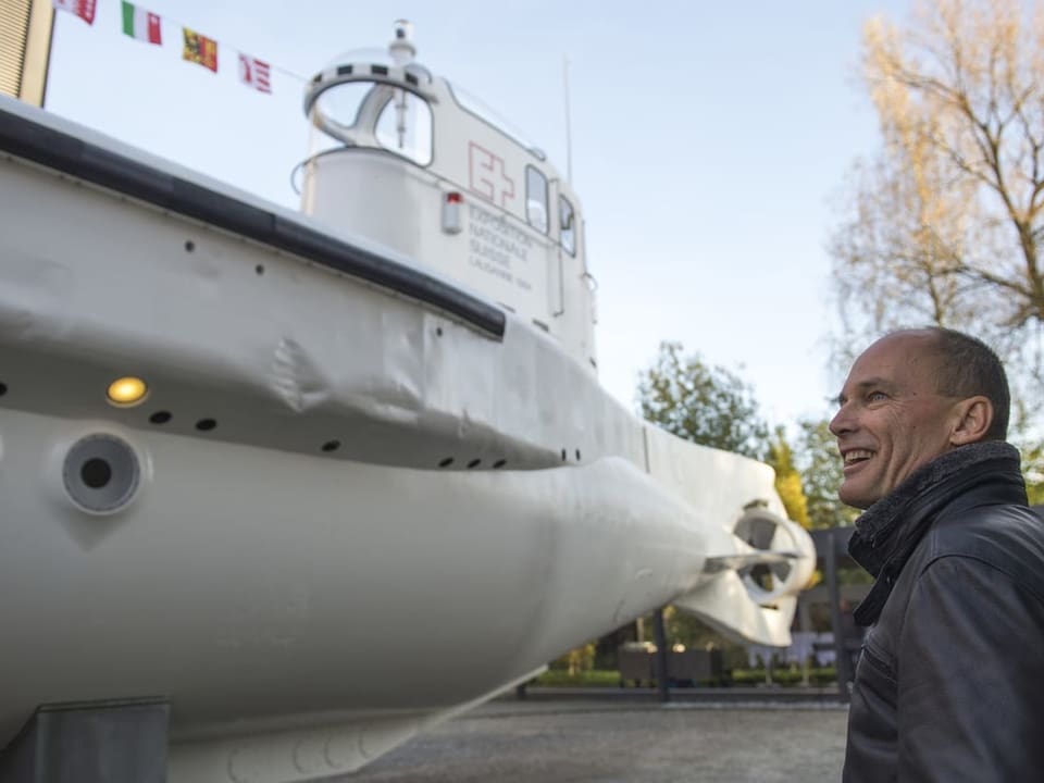 Mann lächelt neben einem weissen U-Boot im Freien.