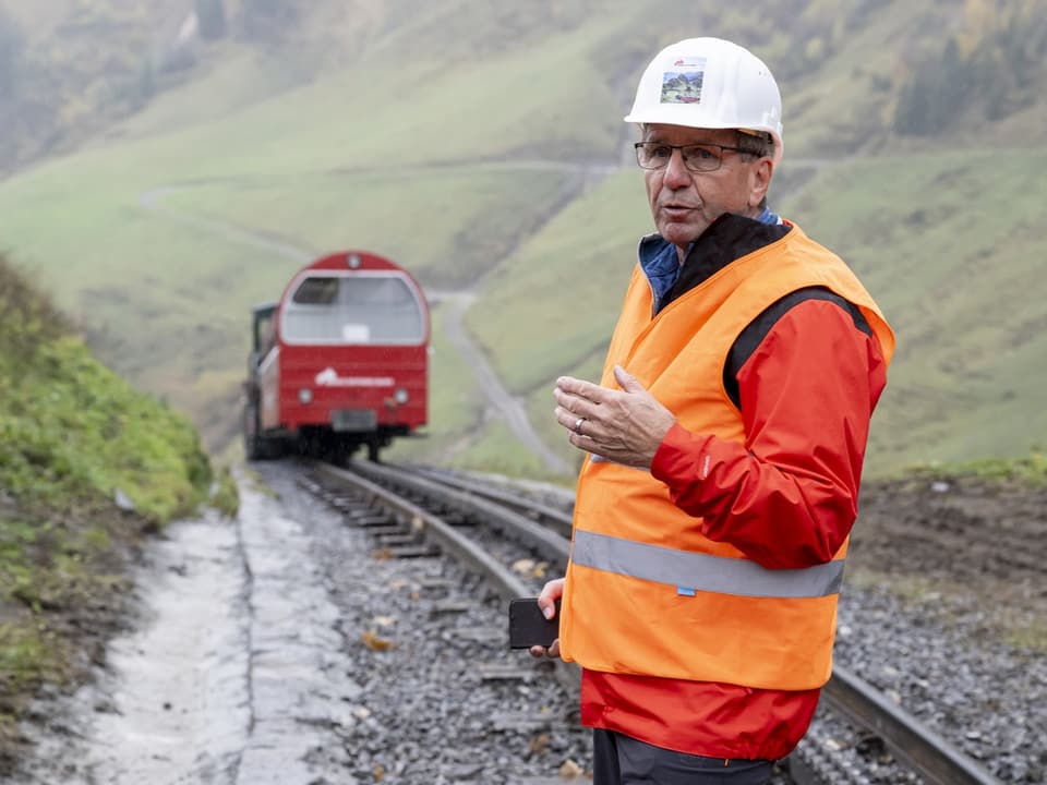 Ein Mann in oranger Weste steht vor einer roten Bahn. 