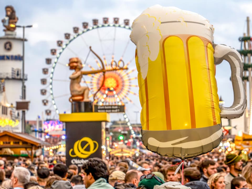 Menschenmenge beim Oktoberfest mit Bierkrug-Ballon und Riesenrad.