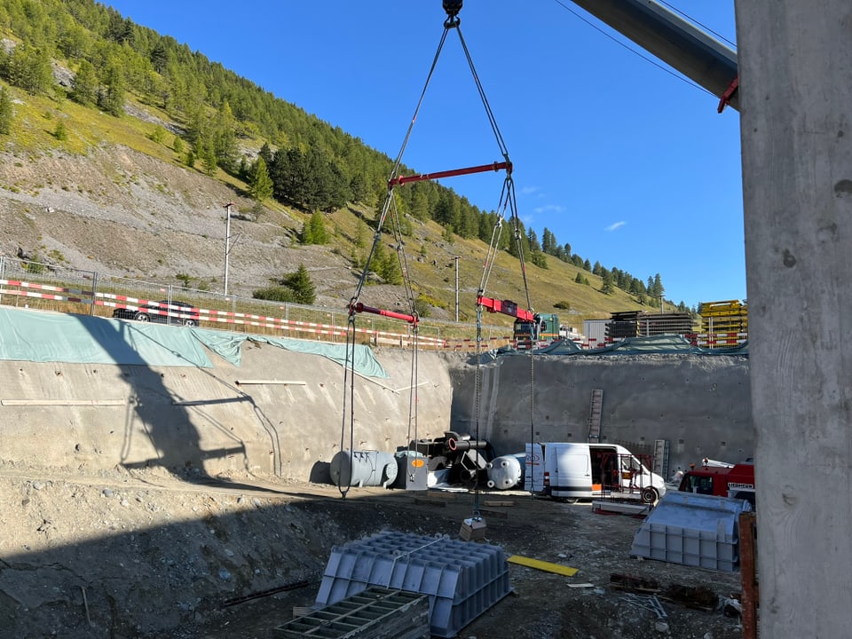 Kran hebt Materialien auf Baustelle in bergigen Landschaft.