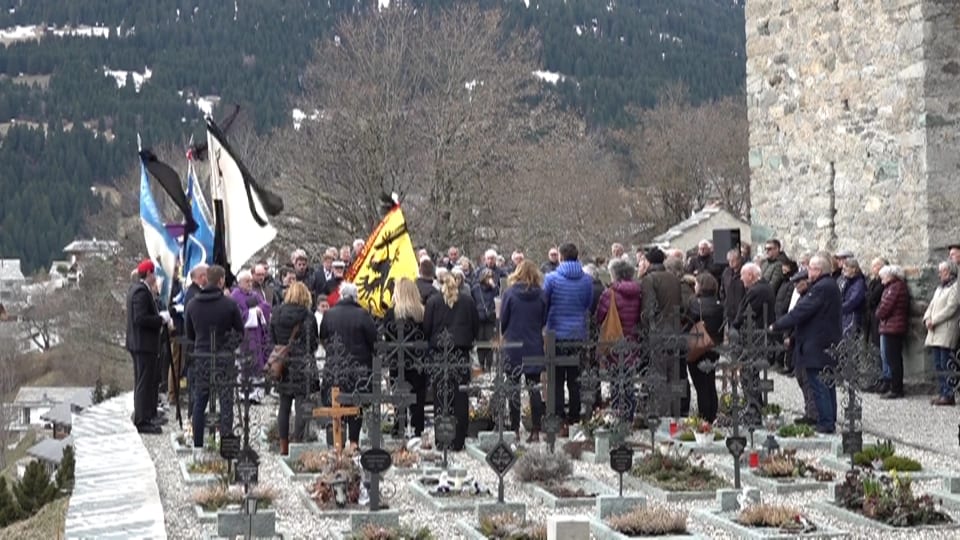 Menschenmenge bei einer Veranstaltung auf einem Friedhof mit Fahnen.