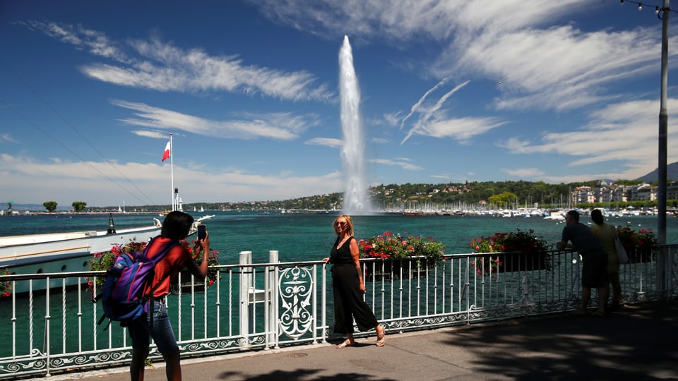 Ein Mann fotografiert eine Frau, sie steht am Genferseeufer mit dem Jet d'eau im Hintergrund.