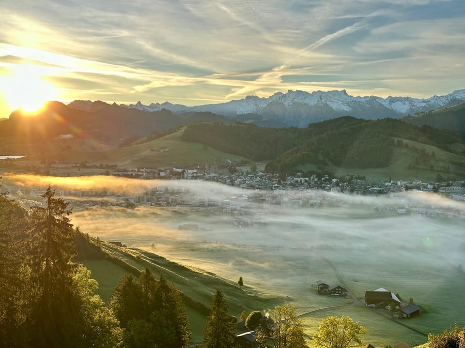 Sonnenaufgang über Alpenlandschaft mit Nebel und Dorf.