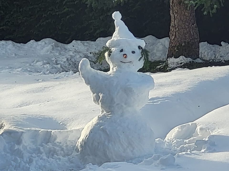 Schneemann mit Mütze im Sonnenschein.