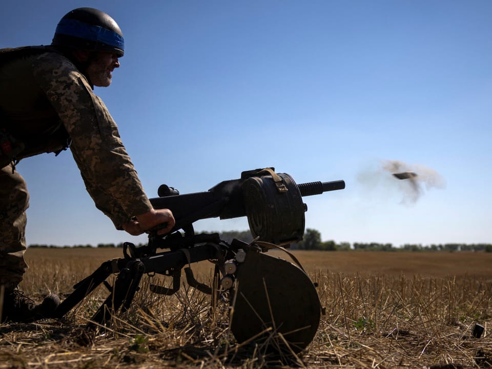 Ukrainischer Soldat beim Abfeuern eines Maschinengewehrs auf freiem Feld.