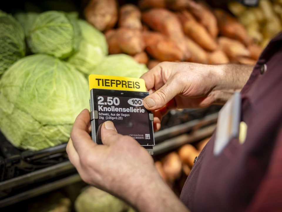 Person hält Preisschild für Knollensellerie im Supermarkt.