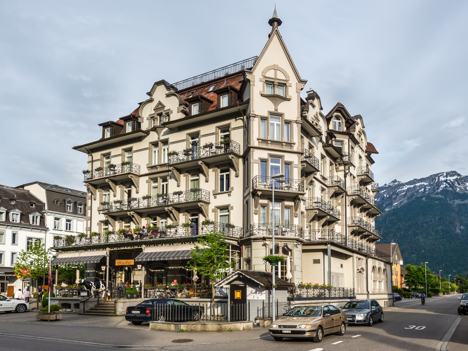 Historisches Gebäude mit Bergblick und parkenden Autos.