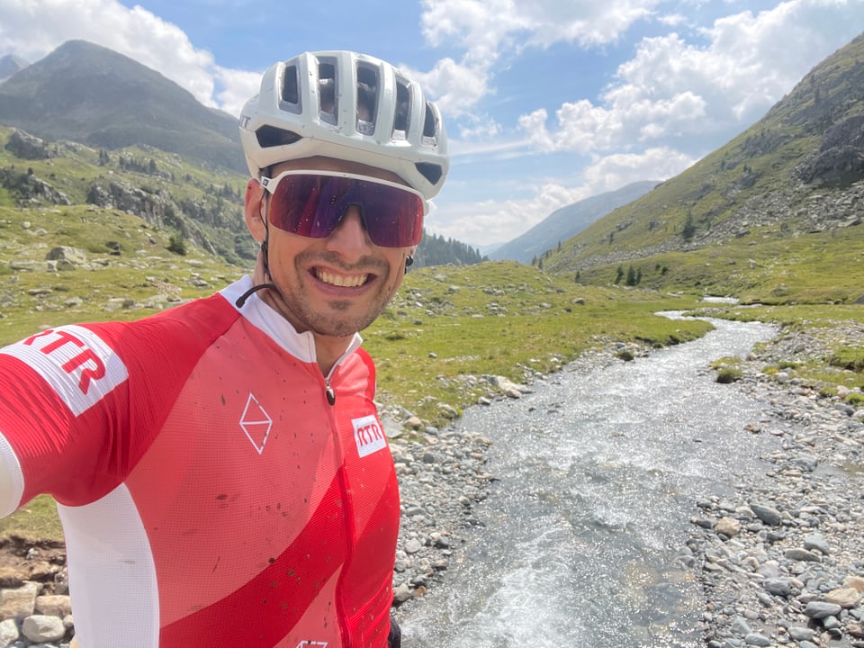 Radfahrer Andreas Wieland in rotem Trikot posiert vor einem Bach in den Bergen.