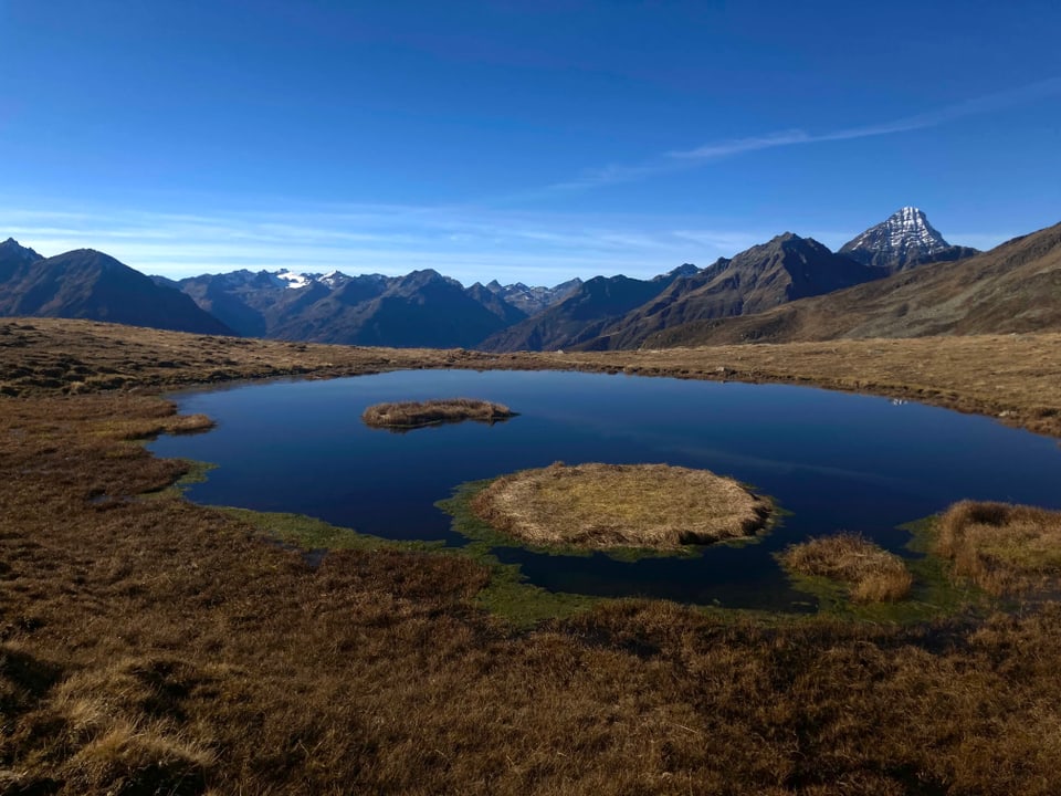 Bergsee mit umliegenden Bergen bei blauem Himmel.