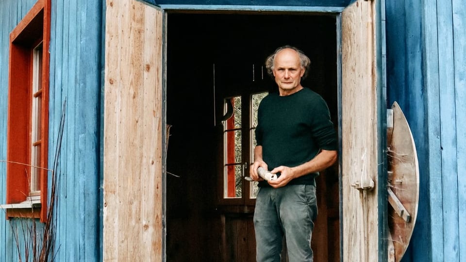 Älterer Mann steht mit Kuhhorn im Eingang eines Schuppens
