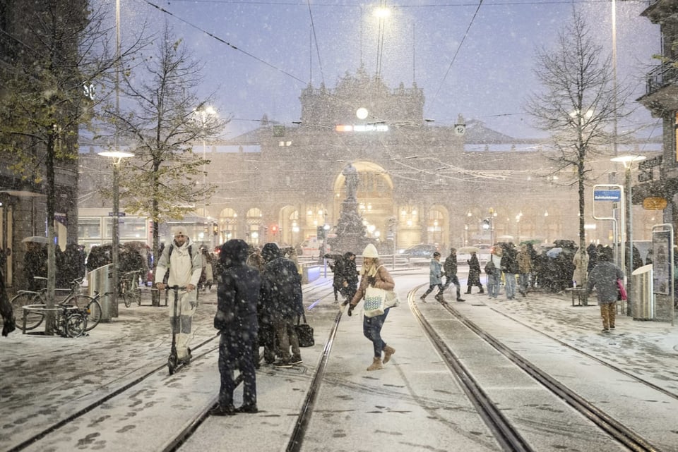 Menschen überqueren verschneite Strassenbahngleise bei Schneefall.