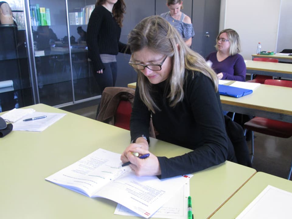 Eine Frau sitzt in einer Schulbank und macht sich Notizen.