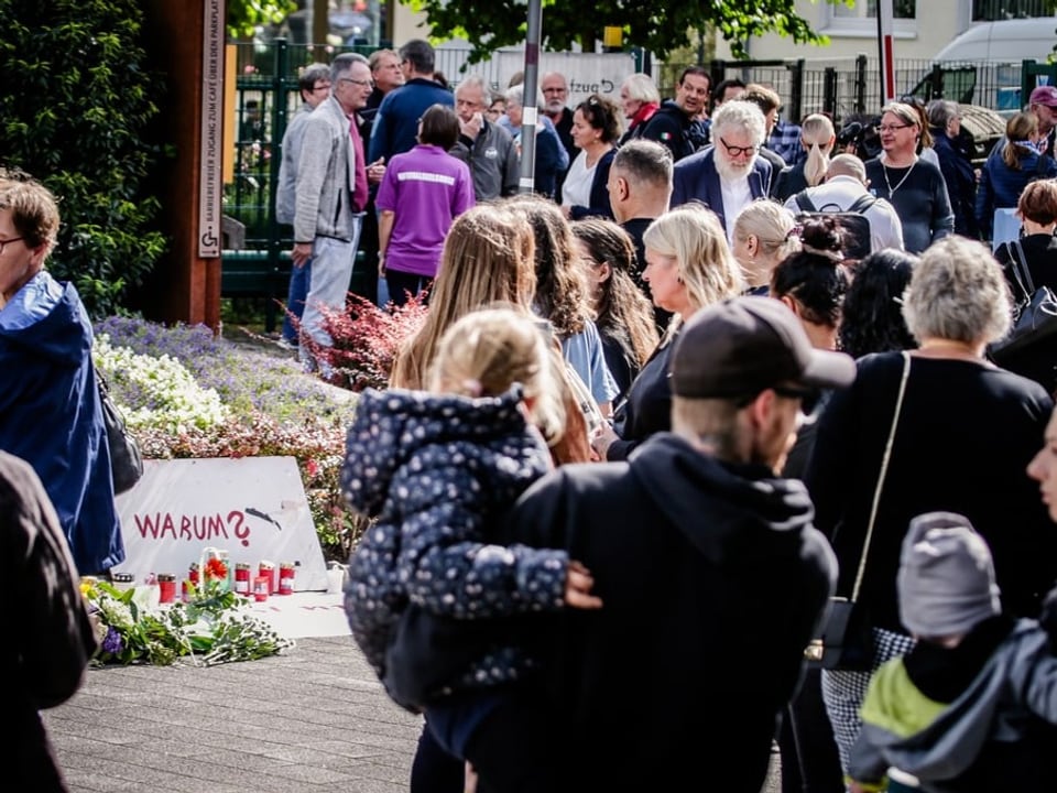 Menschenmenge versammelt sich bei einem Mahnmal mit Blumen und Kerzen.