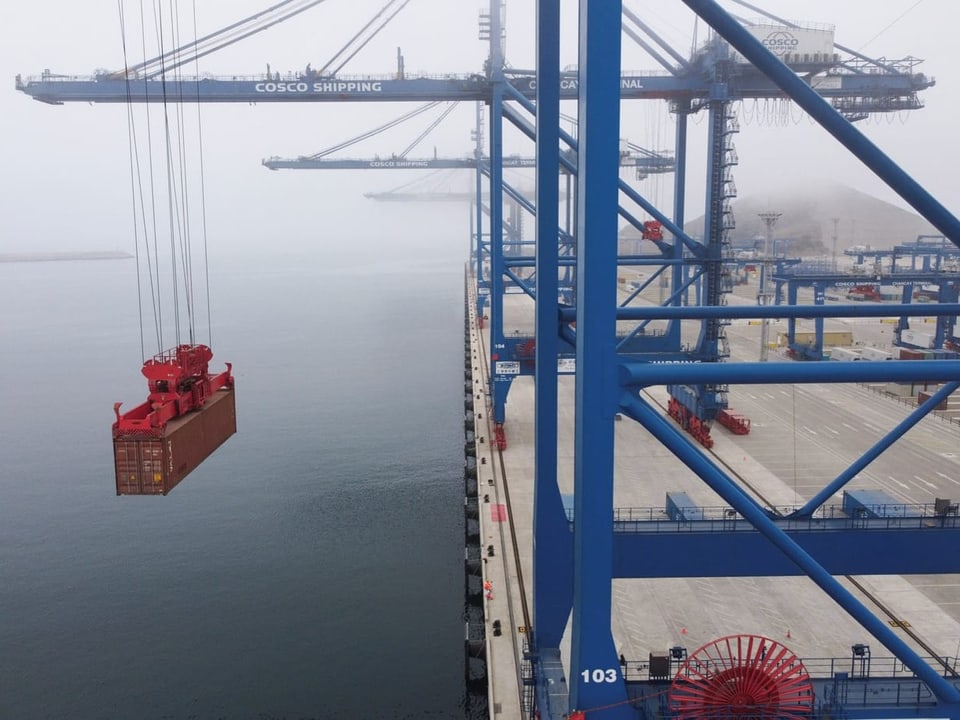 Hafenkran hebt Container über Wasser an nebligem Tag.