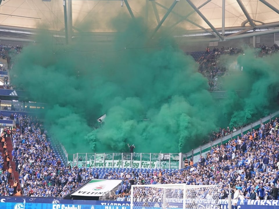 Stadion mit Fans und grünem Rauch.