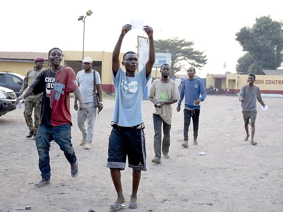 Freigelassene Häftlinge in Kinshasa verlassen das Gefängnis und halten ihre Entlassungspapiere in die Höhe.