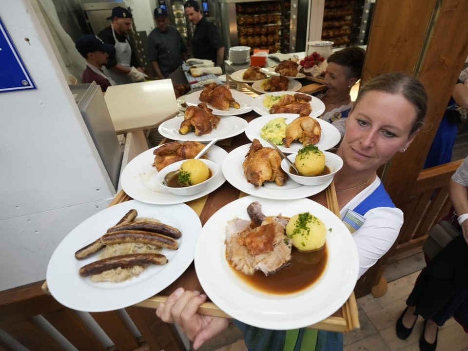 Kellnerin trägt viele Teller mit gebratenem Hähnchen und Würstchen.