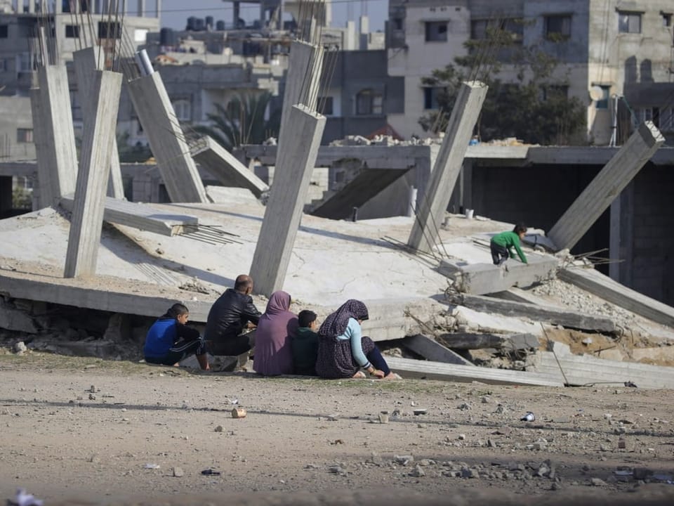 Familie sitzt vor zerstörtem Gebäude im Gazastreifen