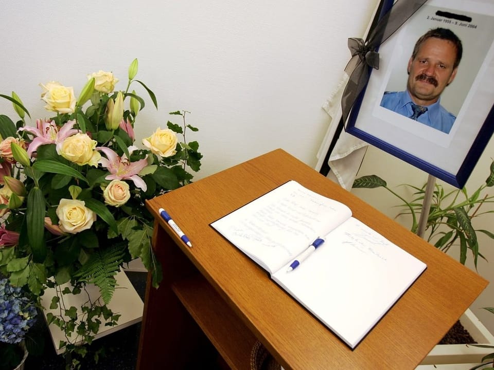 Foto eines Mannes, Blumen und ein Buch sind auf einem Tisch. 