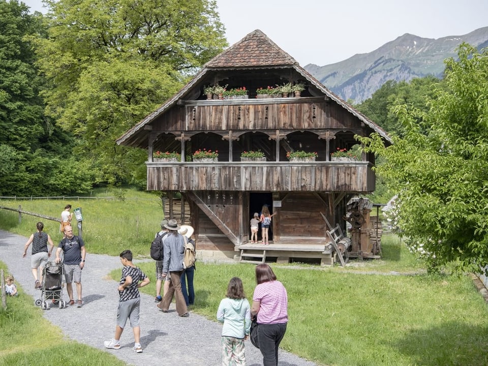 Historisches Holzhaus mit Besuchern in einer grünen Landschaft.