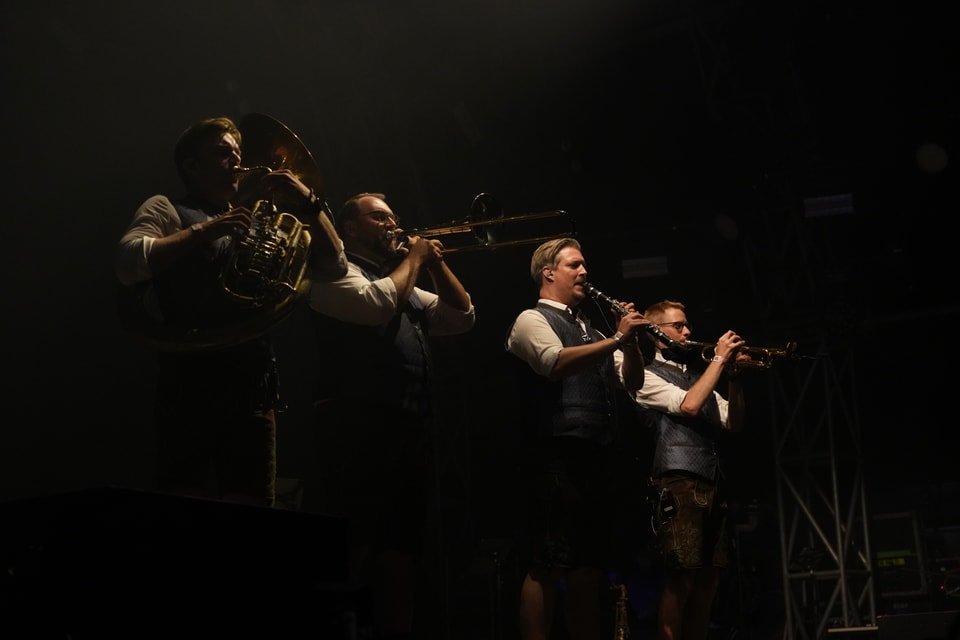 Vier Männer in traditioneller Kleidung spielen Blechblasinstrumente auf einer Bühne am Open Air Lumnezia 2024.