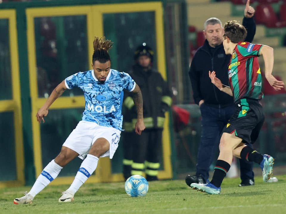 Fussballspieler im blauen Trikot im Dribbling gegen einen Gegenspieler.