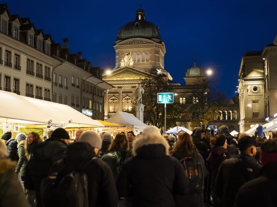 Abendlicher Weihnachtsmarkt mit Menschenmenge vor beleuchteten historischen Gebäuden.