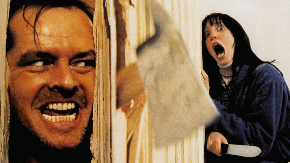 Szene aus einem Horrorfilm mit einem Mann, der durch ein zerbrochenes Türblatt schaut und einer Frau, die schreit.
