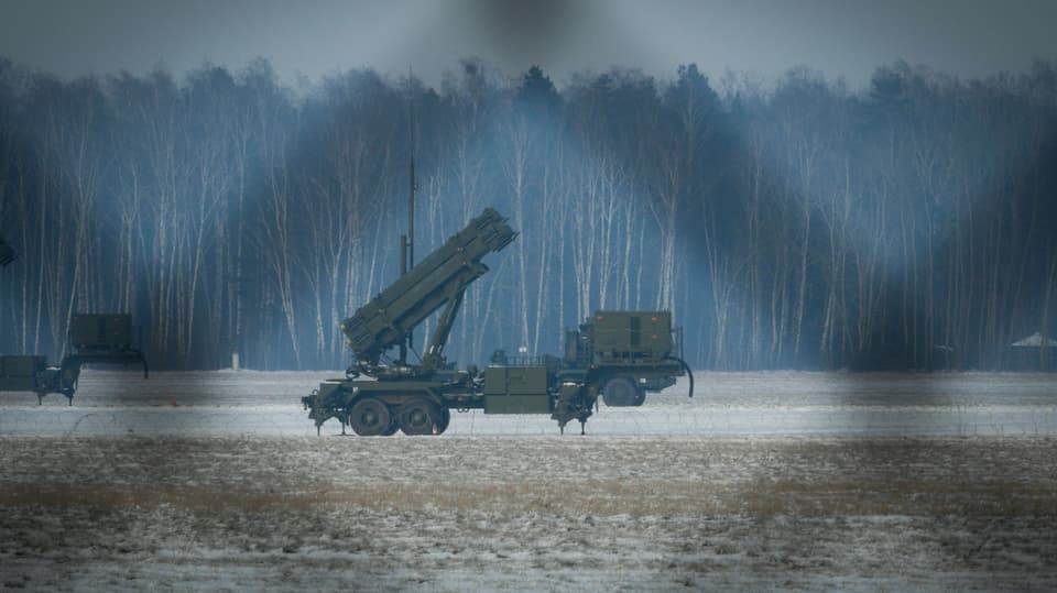 Militärfahrzeug mit Raketenwerfer im verschneiten Feld vor bewaldetem Hintergrund.