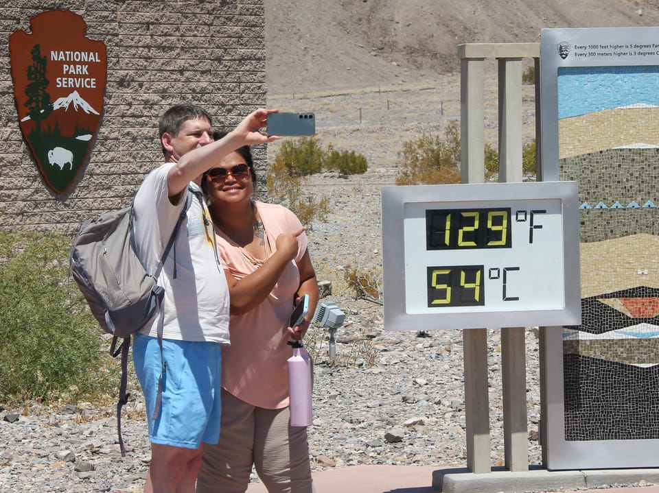 Zwei Besucher machen ein Selfie vor einem Temperaturschild im Nationalpark.