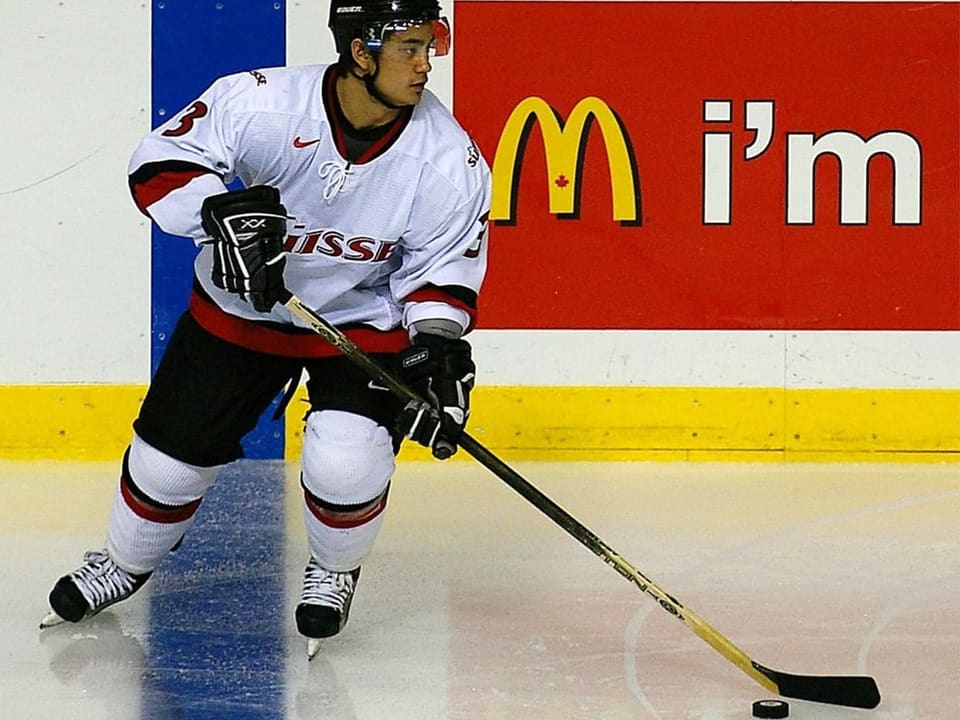 Eishockeyspieler in weissem Trikot mit Puck auf dem Eis.