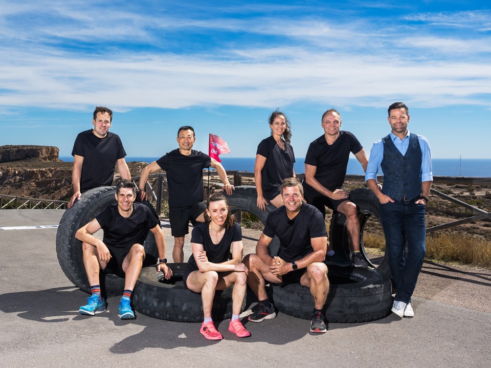 Gruppe von acht Menschen in Sportkleidung steht vor grossen Reifen im Freien.