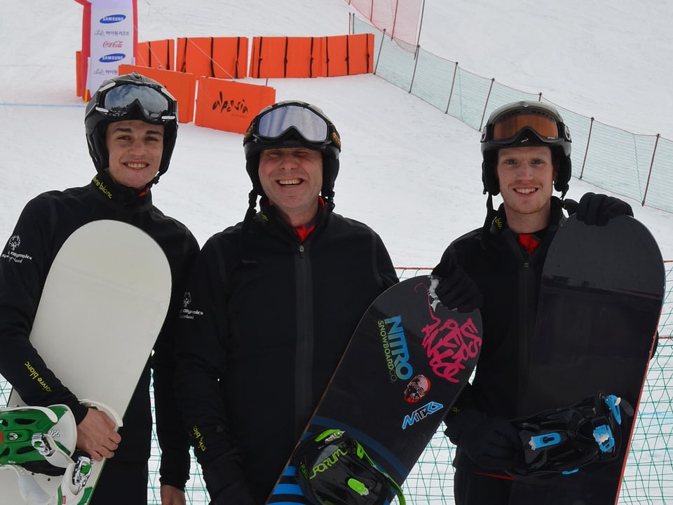 Cyrill von Mentlen  steht mit Snowboard zwischen zwei Männern im Zielgelände.