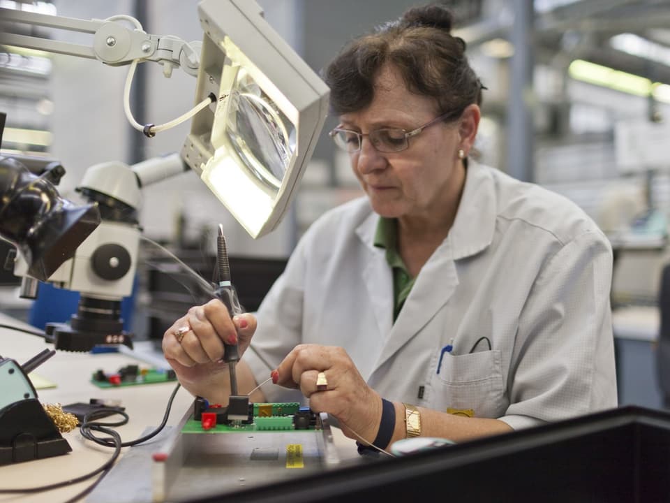 Frau in Laborkittel arbeitet an elektronischen Komponenten.