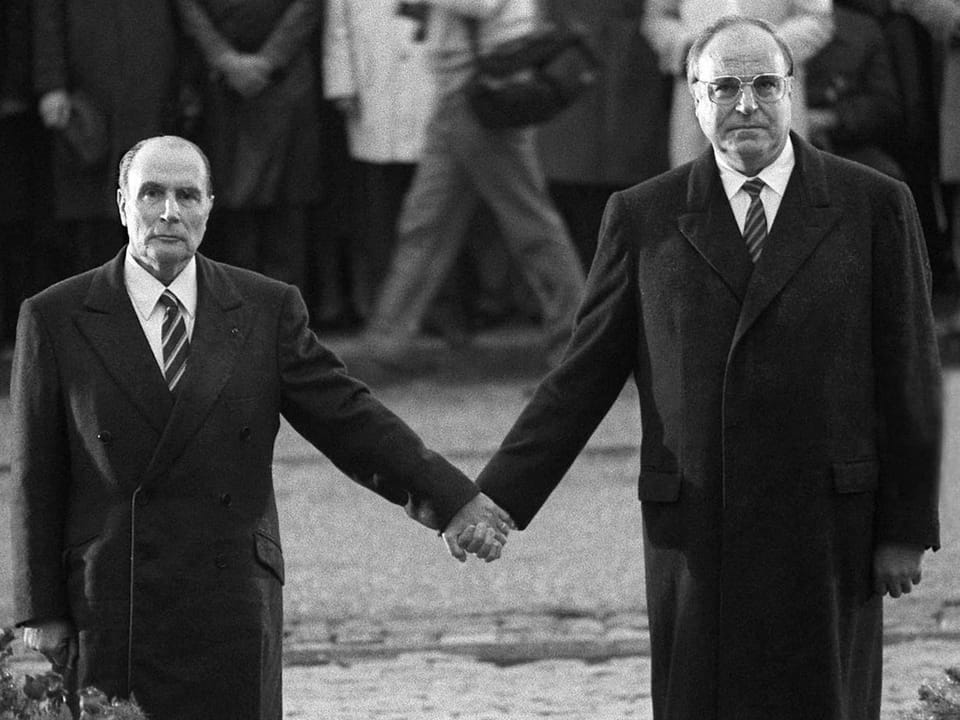 Zwei Männer in Anzügen halten Händchen bei einer öffentlichen Veranstaltung.