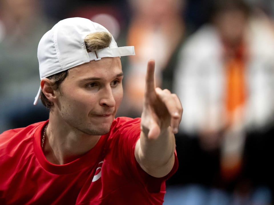 Tennisspieler in rotem Shirt und weisser Kappe zeigt nach vorne.