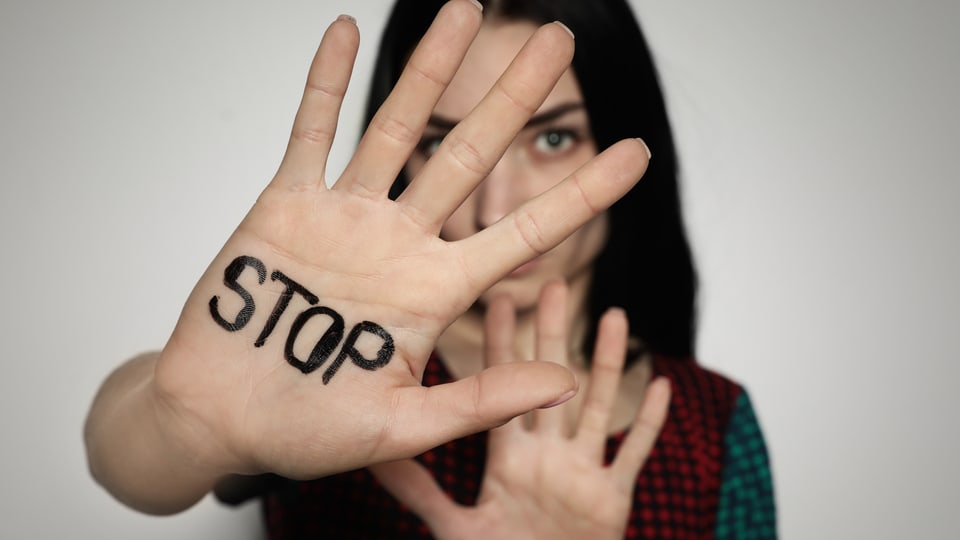 Eine Frau hält die Hände ausgestreckt vor sich hin, als suche sie Schutz. Auf der einen Hand steht «STOP».