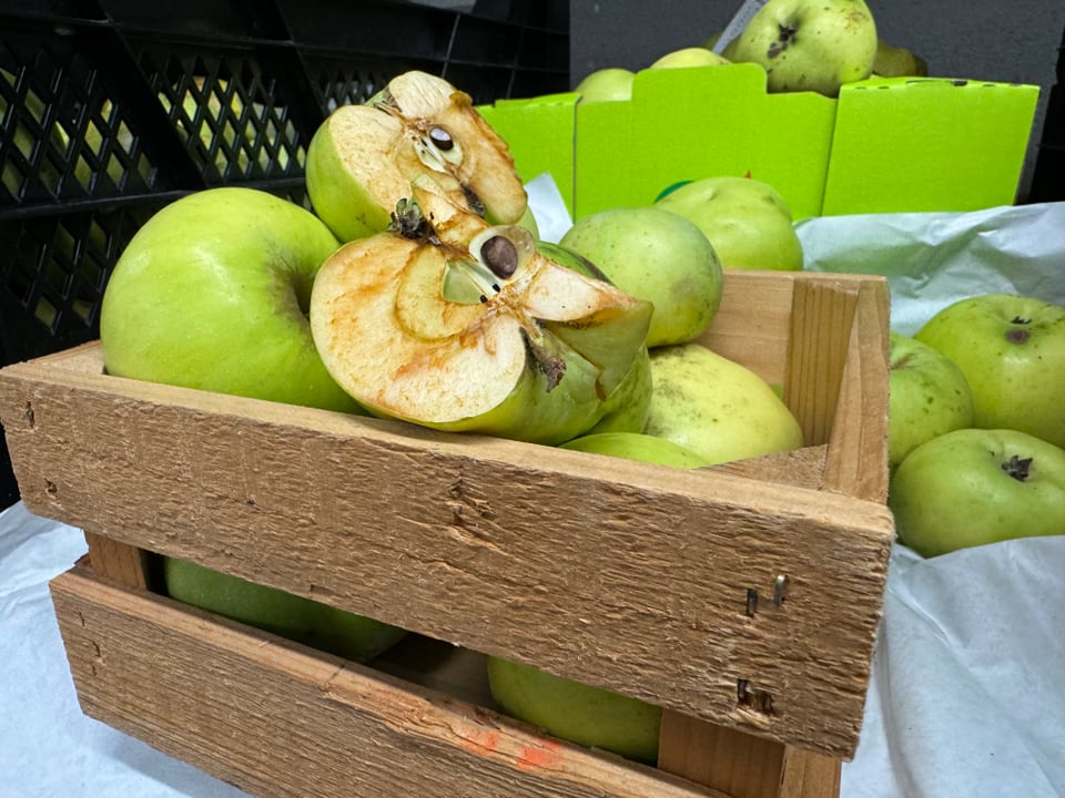 Ein Holzkorb mit grünen Quitten, eine durchgeschnitten.