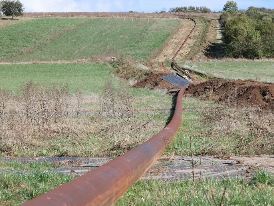 Rostiges Rohr entlang eines Hügels in grüner Landschaft.