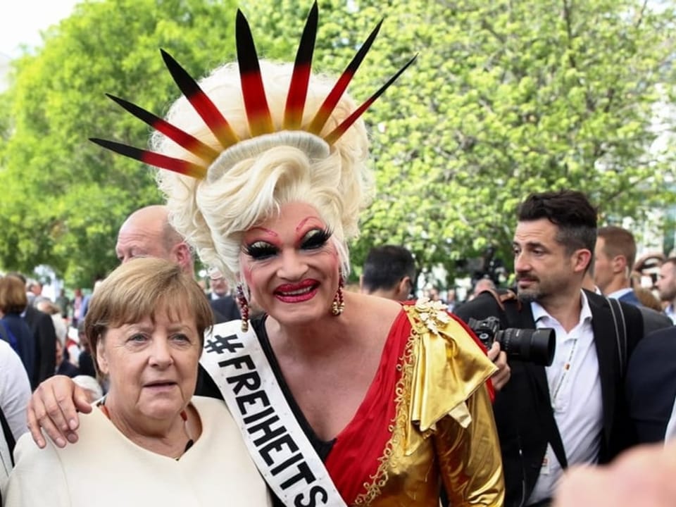 Angela Merkel neben einer Frau mit einem Strahenkranz wie den der US-Freiheitsstatue. Die Strahlen sind gelb-rot-schwarz