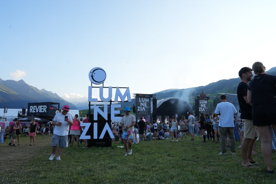 Menschen bei Musikfestival Lumnezia im Freien vor Gebirgskulisse am Open Air Lumnezia 2024.